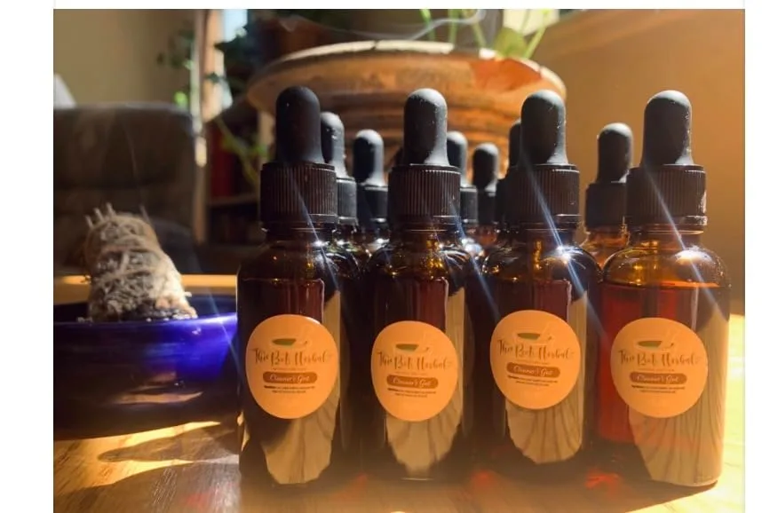 Customer photo of four amber glass dropper bottles with orange labels arranged on a wooden surface indoors.