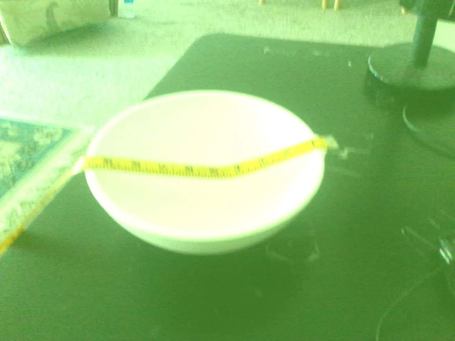 Customer photo of a white ceramic crucible with yellow measuring tape across it on green surface